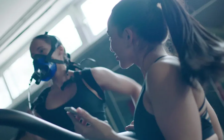 Two people running on treadmills during a metabolic test, one wearing an analysis mask.